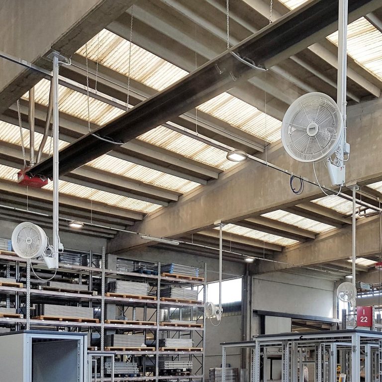 Helle Lagerhalle mit Regalen, an der Decke montierten Ventilatoren und großen Fenstern.